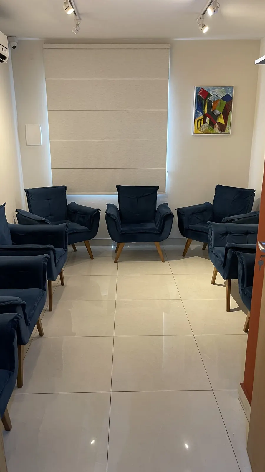 Sala de espera com poltronas azuis, cortina clara e obra de arte